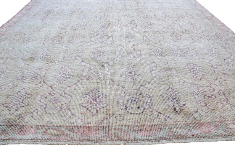 May include: A vintage rug with a cream background and a delicate floral pattern in shades of pink and white. The rug has a fringed edge.