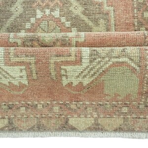 Può includere: Un tappeto vintage con una combinazione di colori rosa e beige sbiaditi. Il tappeto presenta un design persiano tradizionale con dettagli intricati e un bordo con frange.