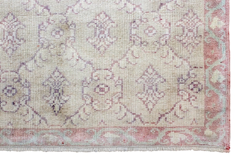 May include: A vintage rug with a cream background and a pink and purple floral pattern. The rug has a fringed edge.