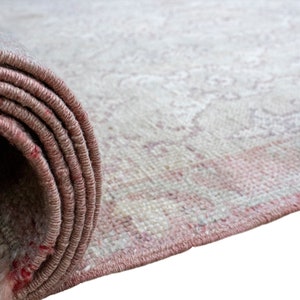 May include: A rolled up rug with a light pink and white pattern. The rug is made of a soft, woven material.
