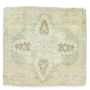 May include: A small, off-white rug with a faded floral pattern in shades of brown, pink, and blue. The rug has a fringed edge.