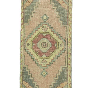 Op de afbeelding: Een roze en beige loper met een geometrisch patroon. De loper heeft een gefranst randje en is gemaakt van wol.