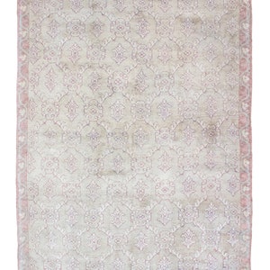 May include: A vintage rug with a light beige background and a repeating pattern of pink and purple floral designs. The rug has a faded, distressed look, giving it a unique and antique feel.