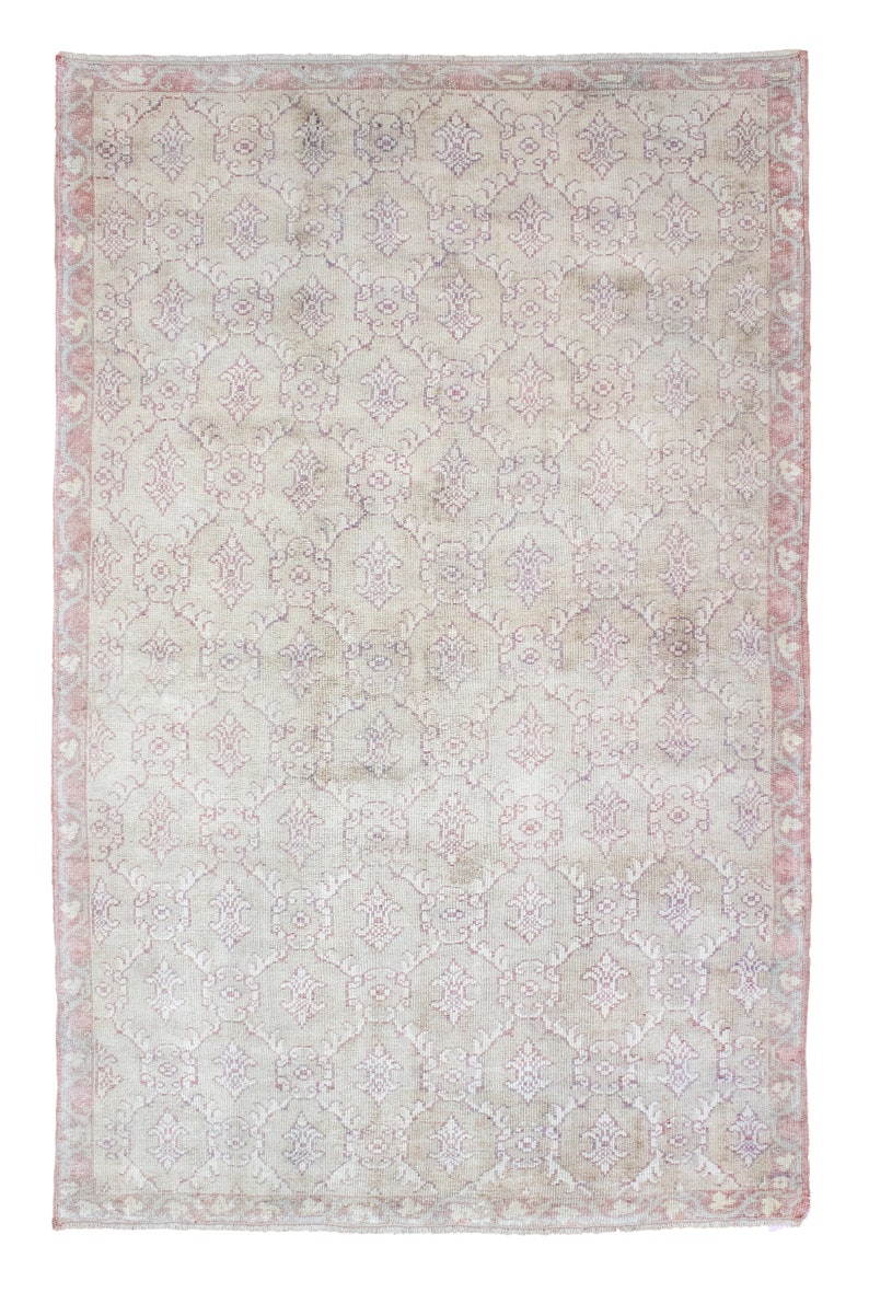 May include: A vintage rug with a light beige background and a repeating pattern of pink and purple floral designs. The rug has a faded, distressed look, giving it a unique and antique feel.