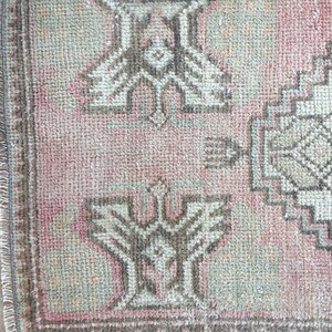 May include: A close-up of a pink and cream colored rug with a geometric pattern. The rug has a fringe border.