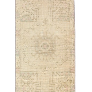 May include: A vintage cream-colored rug with a geometric pattern in shades of beige, light blue, and pink. The rug has a fringed edge.