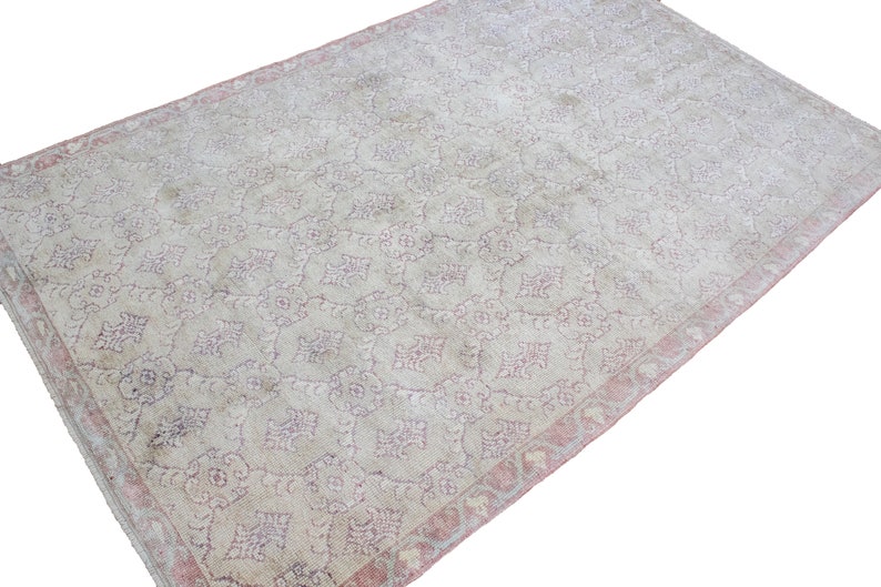 May include: A vintage rug with a light beige background and a delicate pink floral pattern. The rug has a faded, distressed look, giving it a unique and antique feel.