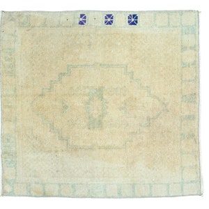 May include: A light beige rug with a light blue geometric pattern and a border. The rug has a faded look and is made of wool.