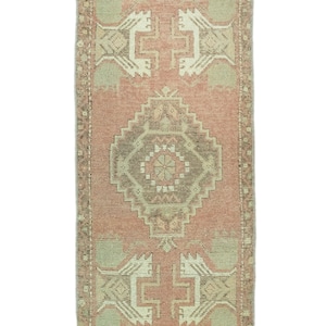 May include: A vintage Turkish runner rug with a pink background and a geometric pattern in shades of brown, beige, and white. The rug has a fringed edge.