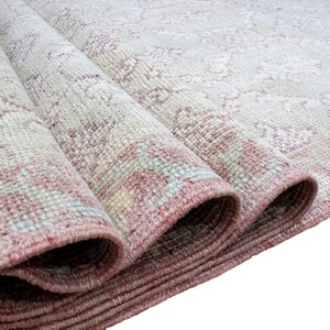 May include: Close-up of a rolled-up rug with a pink and white pattern. The rug has a fringe border and is made of a soft, woven material.