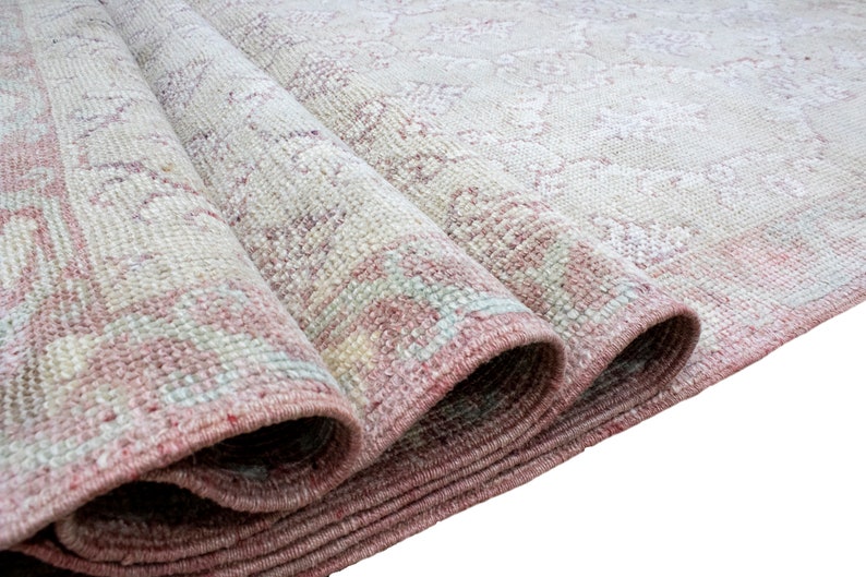 May include: Close-up of a rolled-up rug with a pink and white pattern. The rug has a fringe border and is made of a soft, woven material.
