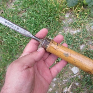May include: A vintage wood handled chisel with a metal blade. The blade is marked "Solingen Germany" and "15".