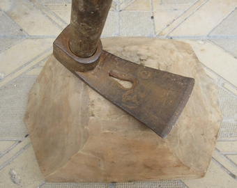 Può includere: Un'ascia in metallo arrugginito con manico in legno, appoggiata su un blocco di legno. L'ascia ha un'apertura a forma di buco della serratura nella lama.