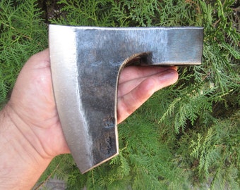 Peut inclure: Une tête de hache en acier forgé à la main avec une lame polie et un corps sombre et texturé. La tête de hache est présentée sur un fond de feuillage vert, mettant en valeur son savoir-faire et son design. La tête de hache est un outil.