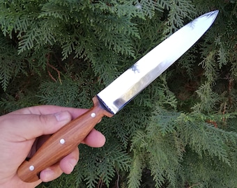 Può includere: Un coltello in acciaio inossidabile con una lama lucida e un manico in legno. Il manico è di colore marrone chiaro ed è fissato con tre rivetti argentati. Il coltello è progettato per l'uso in cucina.