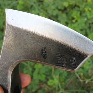 May include: Close-up of a silver axe head with a black handle. The axe head has a small flower-shaped design and the text "Littef" stamped on it.