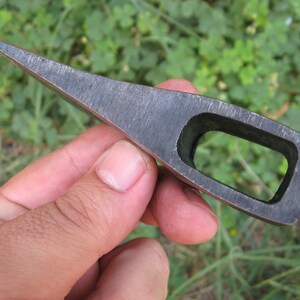May include: A small, hand-forged axe head with a rectangular hole for a handle. The axe head is made of steel and has a sharp edge.