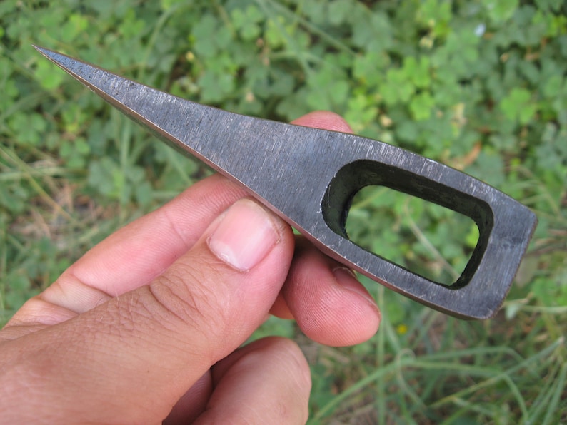 May include: A small, hand-forged axe head with a rectangular hole for a handle. The axe head is made of steel and has a sharp edge.