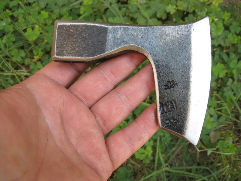 May include: A small, hand-forged axe with a curved blade and a wooden handle. The axe has a black finish and is marked with a symbol and the word "DIY".