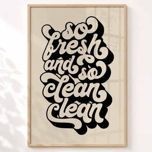 Könnte beinhalten: Ein gerahmter Wandkunstdruck mit dem schwarzen Text "so fresh and so clean clean" in einer fetten, abgerundeten, retro-inspirierten Schriftart. Der Schriftzug ist mit einem schwarzen Schlagschatten auf einem hellbeigen Hintergrund in einem Holzrahmen versehen.