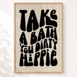 Könnte beinhalten: Ein rechteckiger Wandkunstdruck in einem hellen Holzrahmen mit beigem Hintergrund und fetter, schwarzer, wellenförmiger Typografie im Retro-Stil, die den Text TAKE A BATH You DIRTY HIPPIE zeigt. Der Text ist zentriert und füllt das Bild.