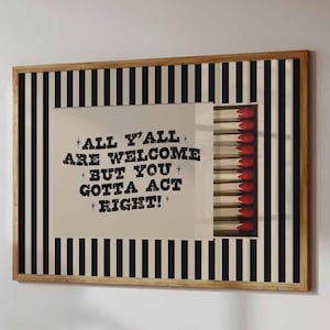 May include: A rectangular framed wall art piece featuring a black and white vertical striped background. The centre displays a matchbox graphic with red-tipped matches and the text: ALL Y'ALL ARE WELCOME BUT YOU GOTTA ACT RIGHT!