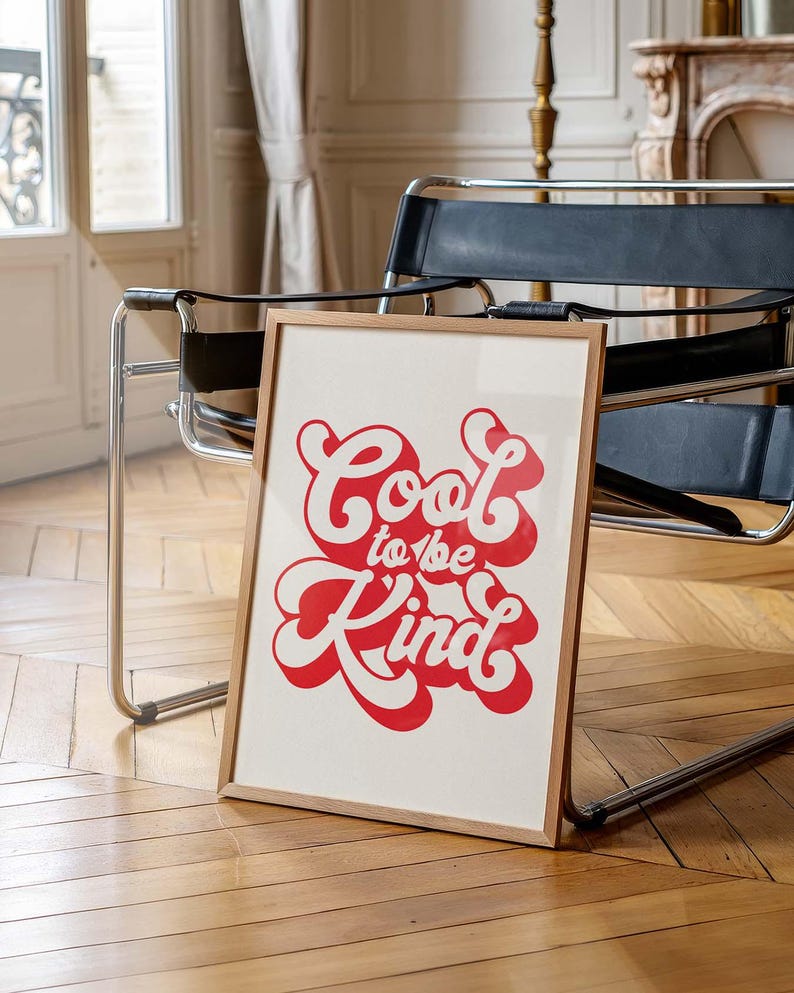K&ouml;nnte beinhalten: Ein rechteckiger gerahmter Druck mit dem Text Cool to be Kind in einer fetten, roten Retro-Schriftart mit wei&szlig;er Umrandung. Das Kunstwerk ist in einem hellen Holzrahmen pr&auml;sentiert und zeigt ein klares Design mit kontrastreicher Typografie.
