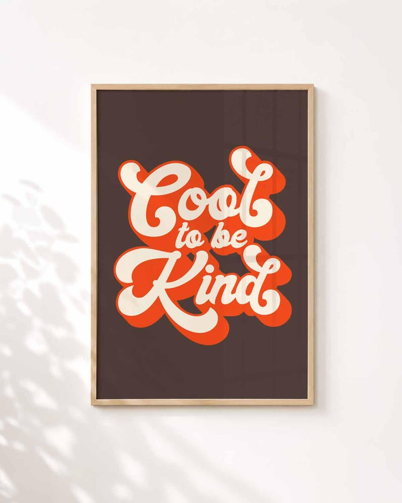 Puede incluir: Una l&aacute;mina decorativa rectangular en un marco de madera clara con el texto Cool to be Kind en una tipograf&iacute;a de color crema con una sombra naranja intensa. Las letras se sit&uacute;an sobre un fondo marr&oacute;n oscuro s&oacute;lido de alto contraste.