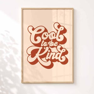 Puede incluir: Una l&aacute;mina decorativa rectangular en un marco de madera clara con el texto Cool to be Kind en una tipograf&iacute;a retro de color naranja oscuro. Las letras tienen una sombra paralela naranja oscuro sobre un fondo beige claro.