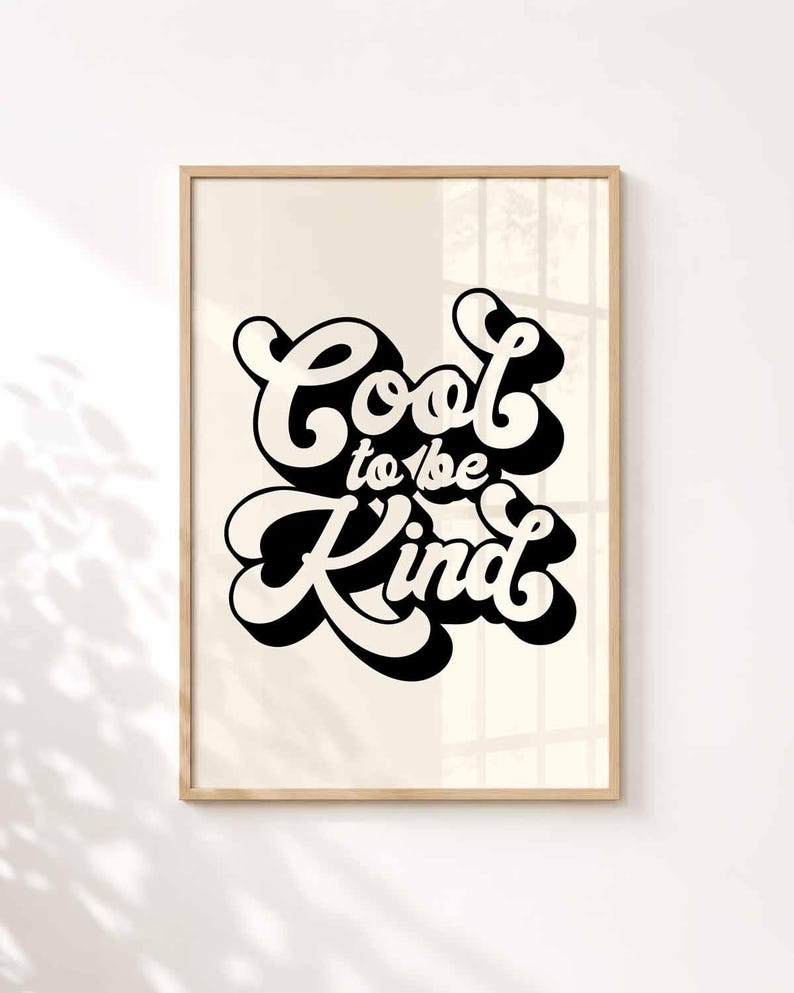 K&ouml;nnte beinhalten: Ein rechteckiger Wandkunstdruck in einem hellen Holzrahmen mit dem schwarzen Schriftzug Cool to be Kind in einer fetten, retro-inspirierten Schriftart mit Schlagschatteneffekt. Der Schriftzug ist auf einem cremefarbenen Hintergrund zentriert.
