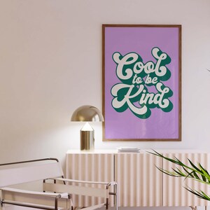Puede incluir: Una l&aacute;mina de arte mural rectangular en un marco de madera con el texto Cool to be Kind en una fuente blanca, negrita y redondeada con una sombra paralela verde oscuro, sobre un fondo liso de color violeta claro, expuesta en una pared.