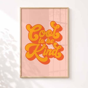 K&ouml;nnte beinhalten: Ein rechteckiges Wandbild in einem hellen Holzrahmen mit einem zartrosa Hintergrund. Der Text "Cool to be Kind" ist mittig in einer fetten, abgerundeten Schriftart in Orange und Gelb mit einem Schlagschatten-Effekt dargestellt.