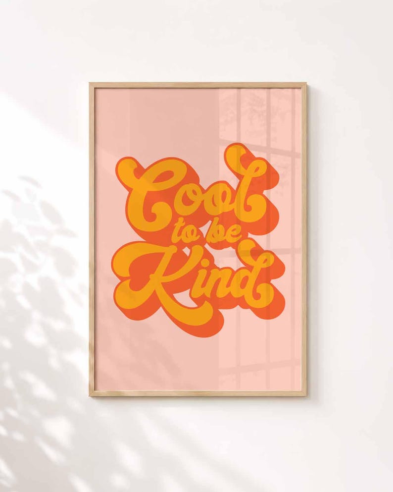 K&ouml;nnte beinhalten: Ein rechteckiges Wandbild in einem hellen Holzrahmen mit einem zartrosa Hintergrund. Der Text "Cool to be Kind" ist mittig in einer fetten, abgerundeten Schriftart in Orange und Gelb mit einem Schlagschatten-Effekt dargestellt.