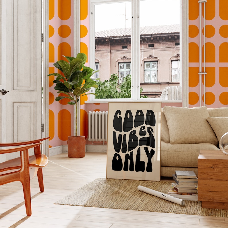 May include: A living room with orange and pink patterned wallpaper, a large plant, a brown sofa, and a black and white poster with the text "Good Vibes Only".