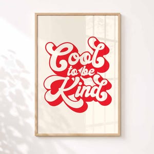 K&ouml;nnte beinhalten: Ein rechteckiger Wandkunstdruck in einem hellen Holzrahmen mit dem Text Cool to be Kind in einer fetten, roten Retro-Schriftart mit wei&szlig;er Umrandung und rotem Schlagschatten auf einem einfarbigen, hell cremefarbenen Hintergrund.