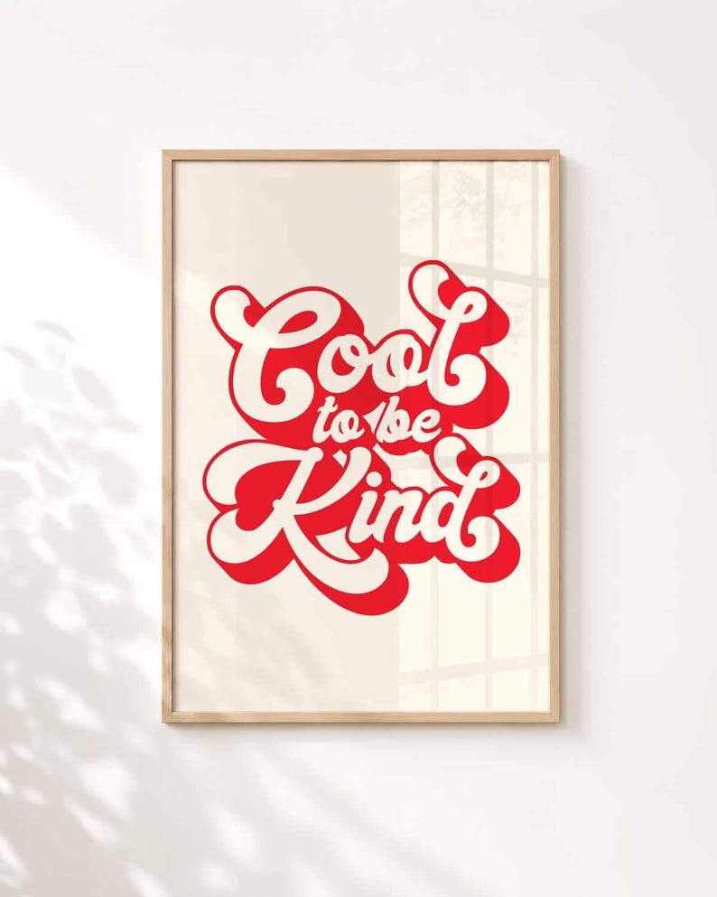 K&ouml;nnte beinhalten: Ein rechteckiger Wandkunstdruck in einem hellen Holzrahmen mit dem Text Cool to be Kind in einer fetten, roten Retro-Schriftart mit wei&szlig;er Umrandung und rotem Schlagschatten auf einem einfarbigen, hell cremefarbenen Hintergrund.