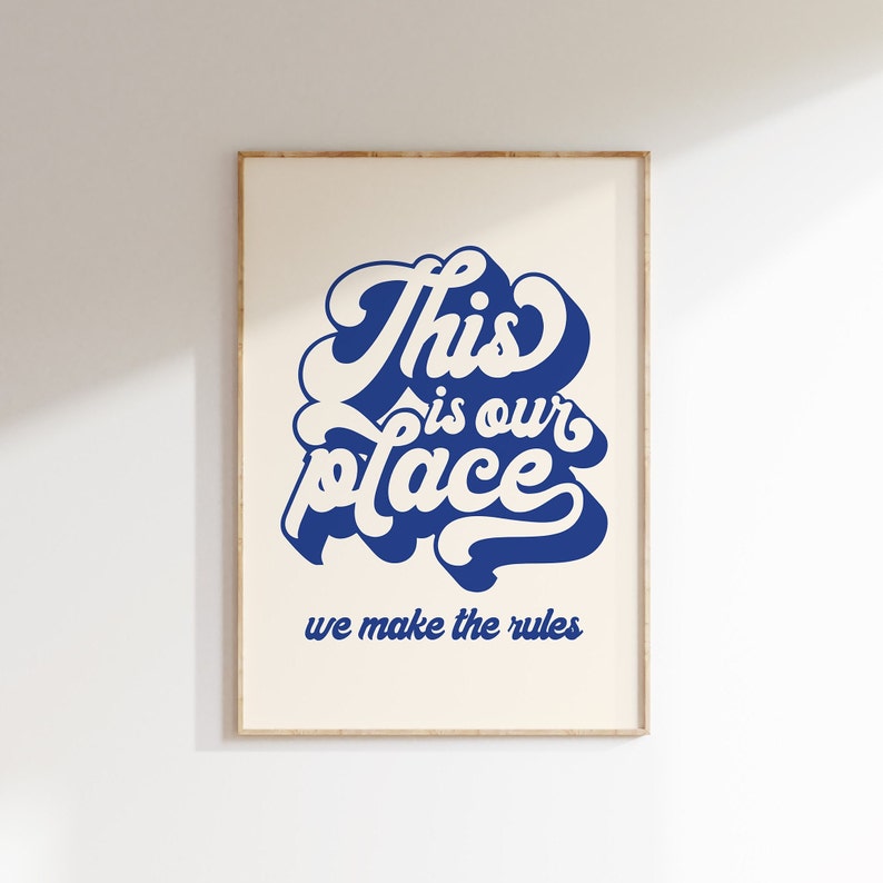 May include: A white and blue typography print with the text "This is our place we make the rules" in a retro style font. The print is framed in a light wood frame.