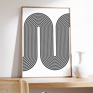 Puede incluir: Impresi&oacute;n de arte abstracto en blanco y negro con un dise&ntilde;o geom&eacute;trico de l&iacute;neas curvas. La impresi&oacute;n est&aacute; enmarcada en un marco de madera claro y est&aacute; colgada en una pared blanca.