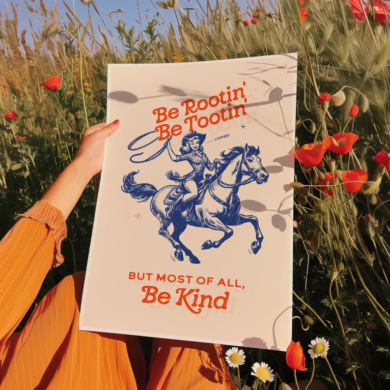 Pu&ograve; includere: Un poster in stile vintage con un'illustrazione blu di una cowgirl a cavallo. Il testo recita "Be Rootin' Be Tootin' - Yippee! But Most Of All, Be Kind."