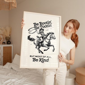 Pu&ograve; includere: Un'illustrazione in bianco e nero di una donna a cavallo con il testo "Be Rootin' Be Tootin' - YIPPEE!" e "But most of all, Be Kind".