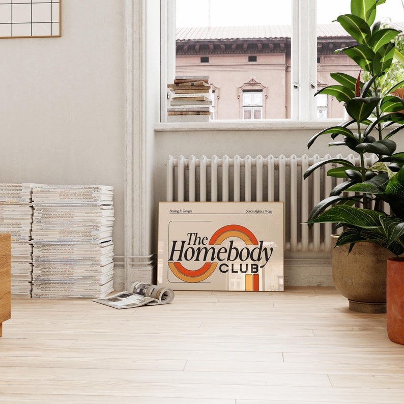 以下が含まれることがあります： レトロなフォントで「The Homebody Club」と書かれたベージュと茶色のポスター。ポスターはオレンジ、イエロー、レッドのストライプの虹のデザインです。