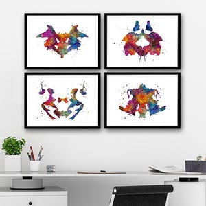 Op de afbeelding: Vier ingelijste aquarelprints met zwarte lijsten. De prints tonen abstracte ontwerpen in levendige kleuren, waaronder blauw, rood, geel en groen. De prints worden weergegeven boven een wit bureau met een zwarte bureaustoel.