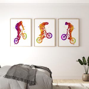 May include: Three watercolor paintings of a person riding a BMX bike. The paintings are in shades of orange, yellow, purple, and blue. The person is silhouetted in the paintings.