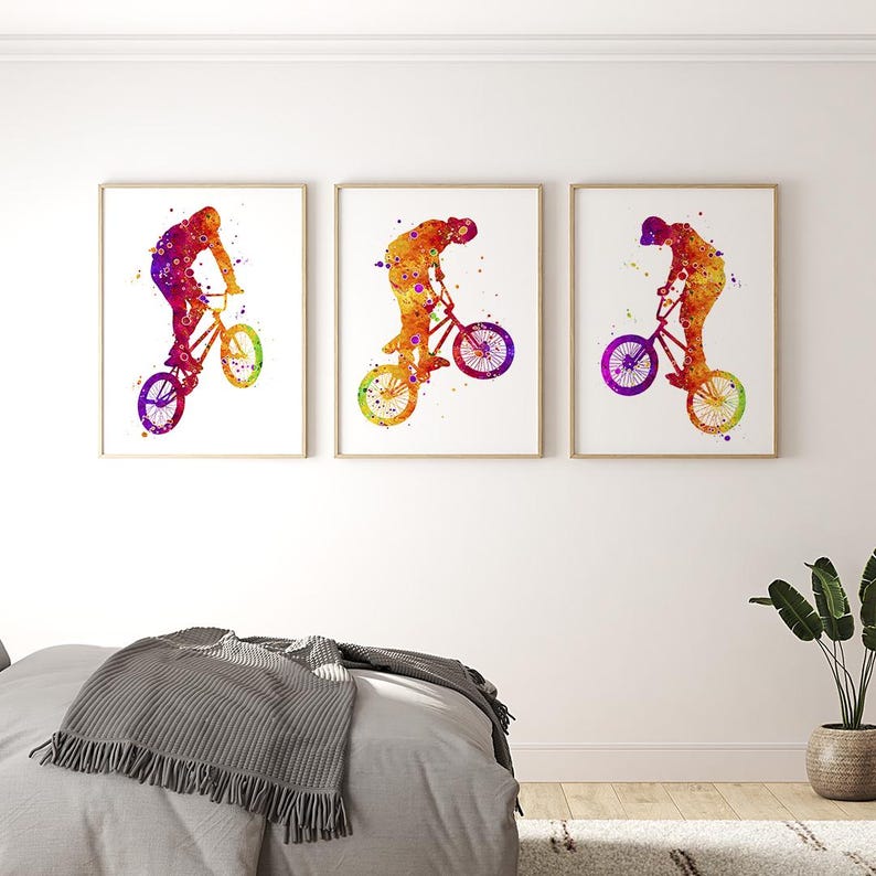 May include: Three watercolor paintings of a person riding a BMX bike. The paintings are in shades of orange, yellow, purple, and blue. The person is silhouetted in the paintings.