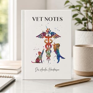 May include: A white hardcover notebook titled VET NOTES with a colorful watercolor illustration of a caduceus symbol flanked by a cat and a dog. The name Dr. Amelia Henderson is printed in black script at the bottom of the front cover.
