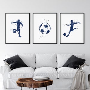 May include: Three watercolor prints featuring a soccer player and a soccer ball. The prints are in shades of blue and white and are framed in black frames.