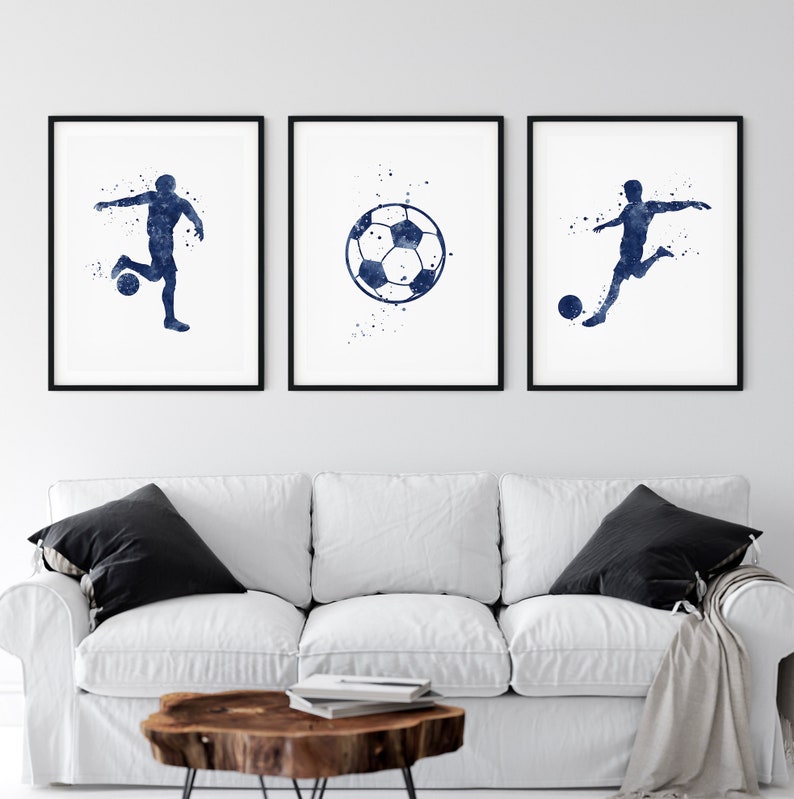 May include: Three watercolor prints featuring a soccer player and a soccer ball. The prints are in shades of blue and white and are framed in black frames.