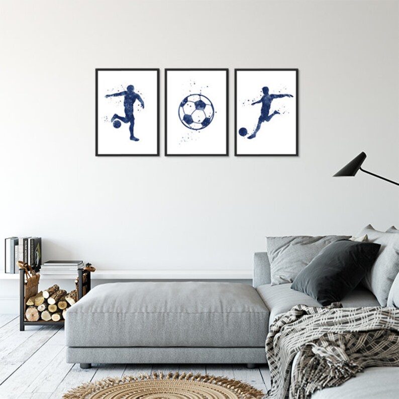 May include: Three framed prints of a soccer player kicking a ball. The prints are in a watercolor style with a blue and white color scheme. The prints are hanging on a white wall above a gray couch.