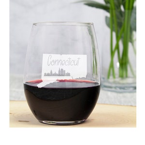 May include: A clear glass wine glass filled with red wine. The glass features a white outline of the state of Connecticut with the word "Connecticut" written on it.