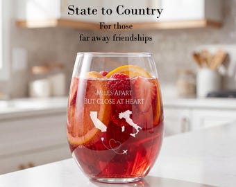 May include: A clear stemless wine glass filled with red liquid, orange slices, and strawberries. The glass features white etched graphics of California and Italy, a heart, an airplane, and the text: MILES APART BUT CLOSE AT HEART.